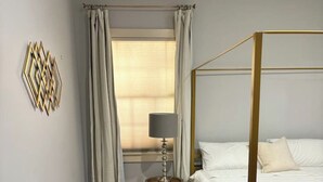 A bedroom with a four-poster bed, a bedside lamp, and a window with curtains. - Cozy King Bedroom w/Bath in Historic Savannah (Savannah)