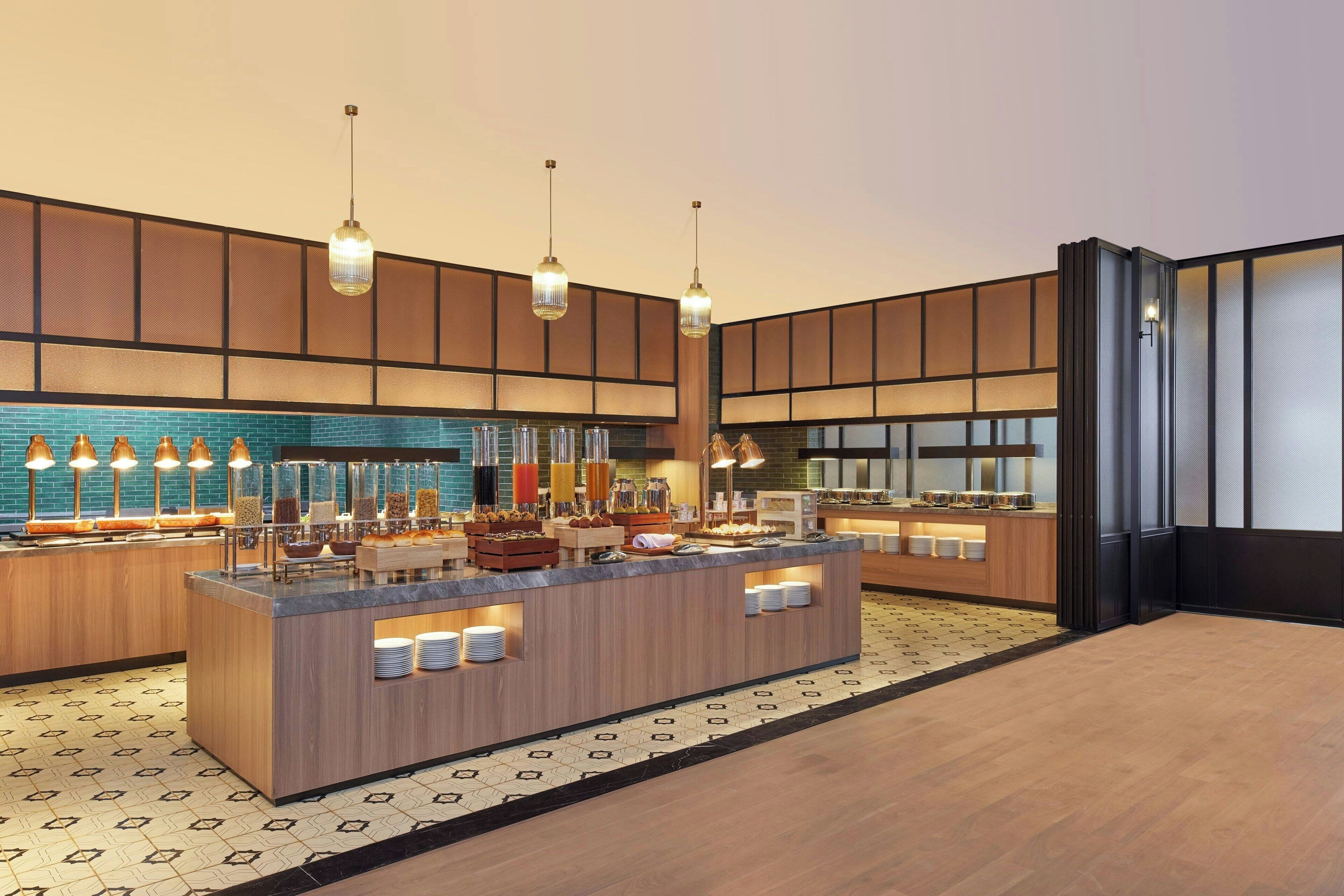 Een moderne hotellobby met een centraal eilandbalie, hanglampen en een patroon vloer.