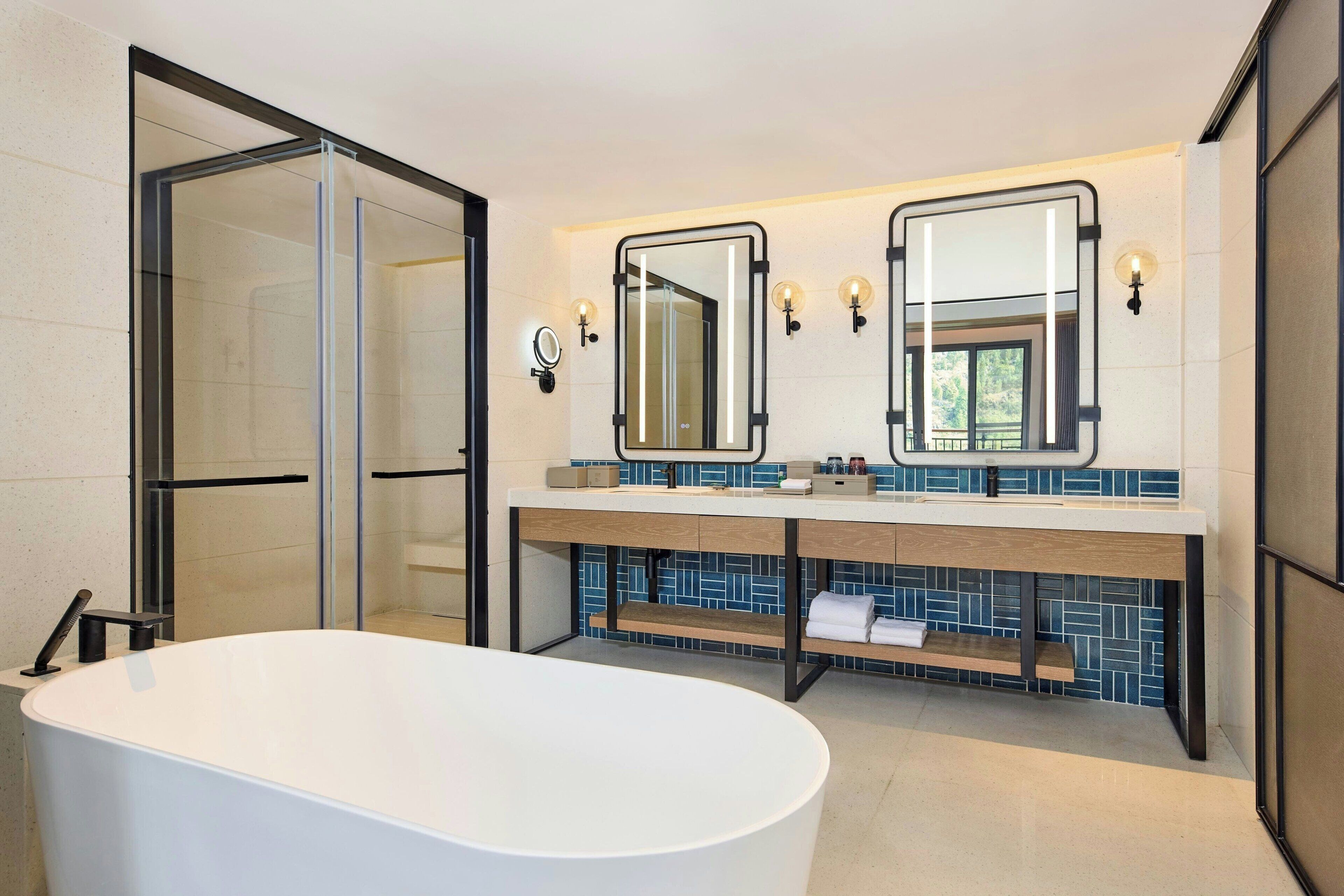 Een moderne badkamer met een vrijstaand bad, een douchecabine van glas en een wastafel met twee spiegels en een wasbak.