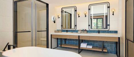 Een moderne badkamer met een vrijstaand bad, een douchecabine van glas en een wastafel met twee spiegels en een wasbak.