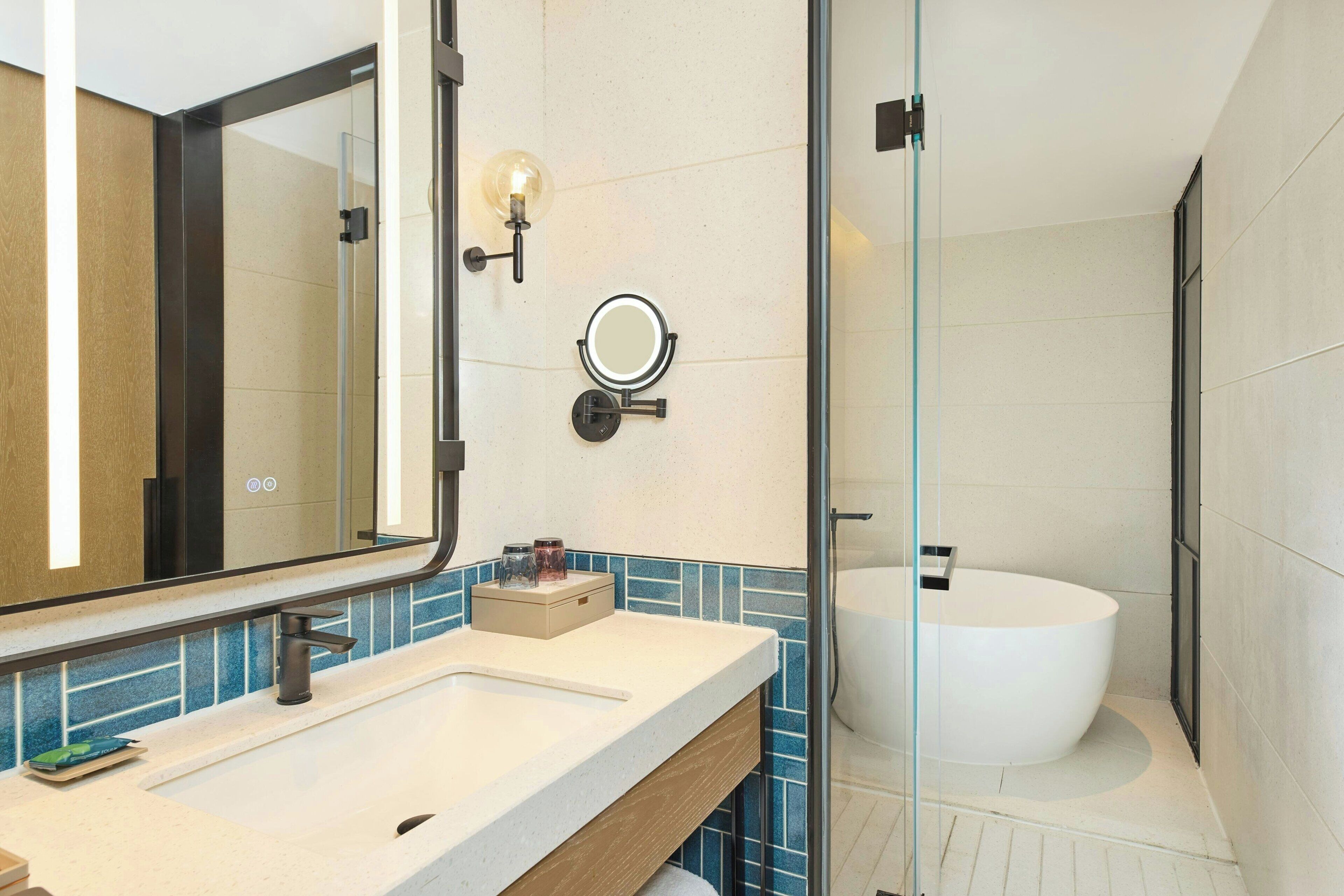 A modern bathroom with a large mirror, a round vanity, a bathtub, and a glass shower enclosure.