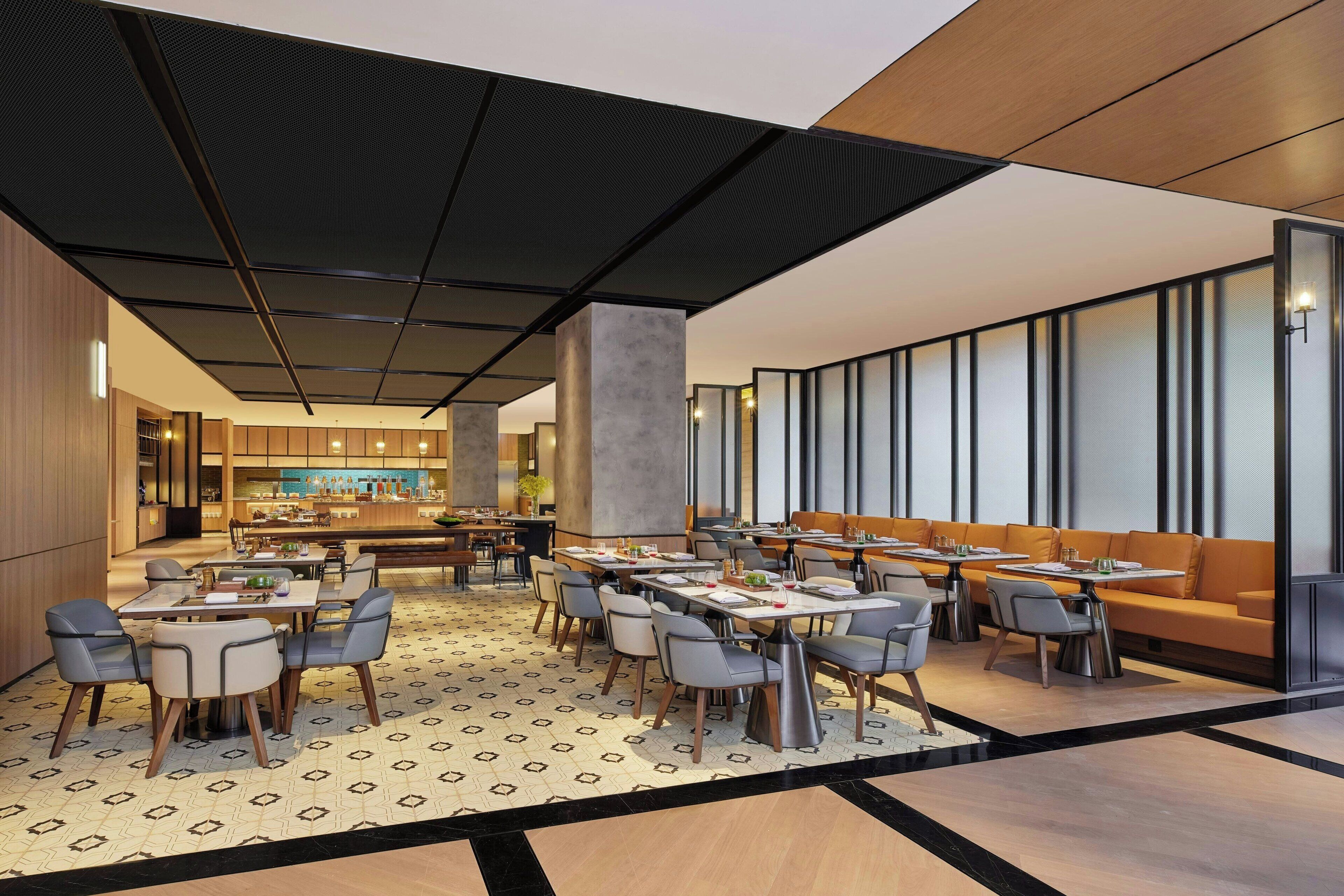 A modern dining area with multiple tables and chairs, a central bar, and a patterned floor.