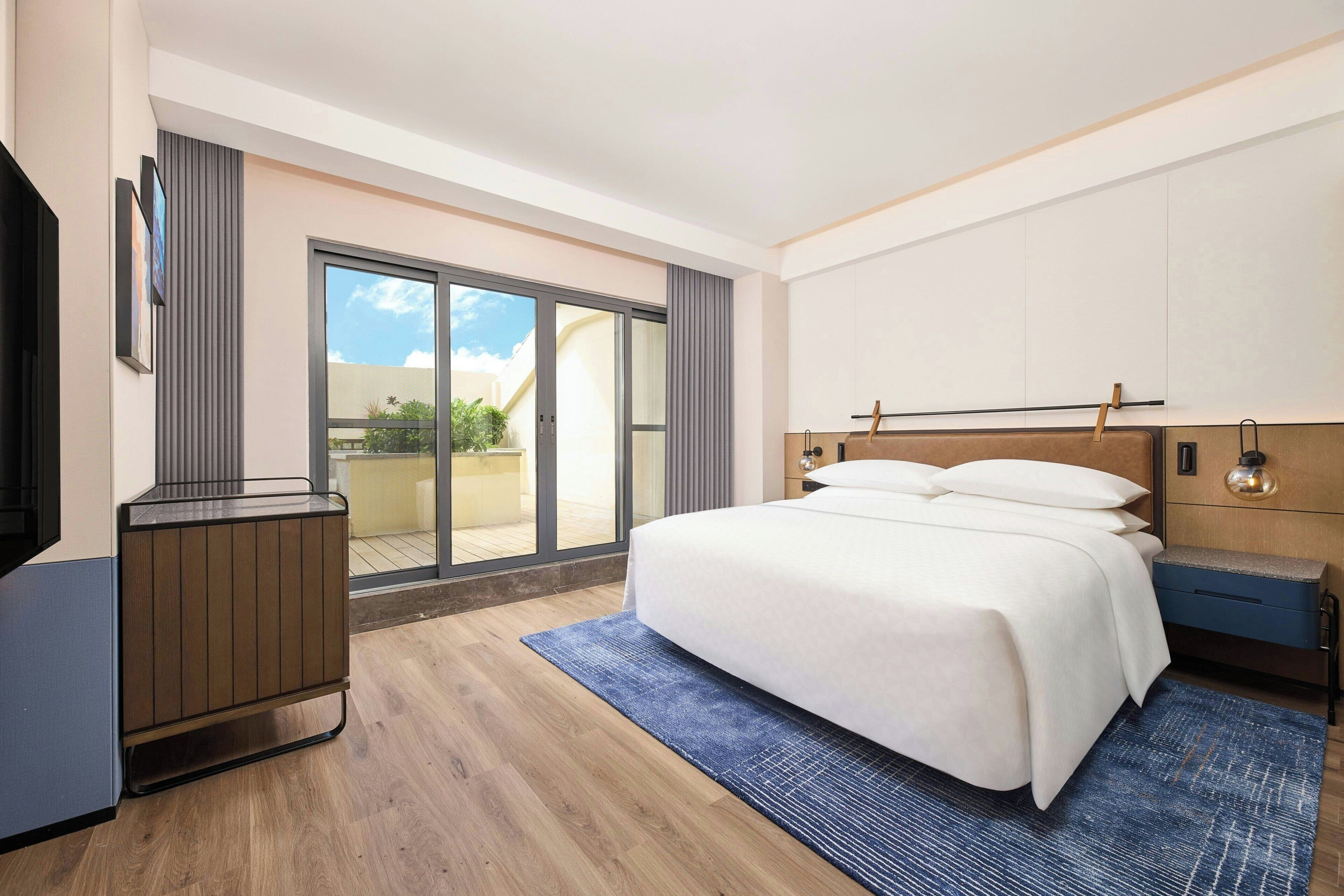 Una habitación de hotel moderna con una cama grande, un escritorio y una puerta de cristal corredera que da a un balcón.