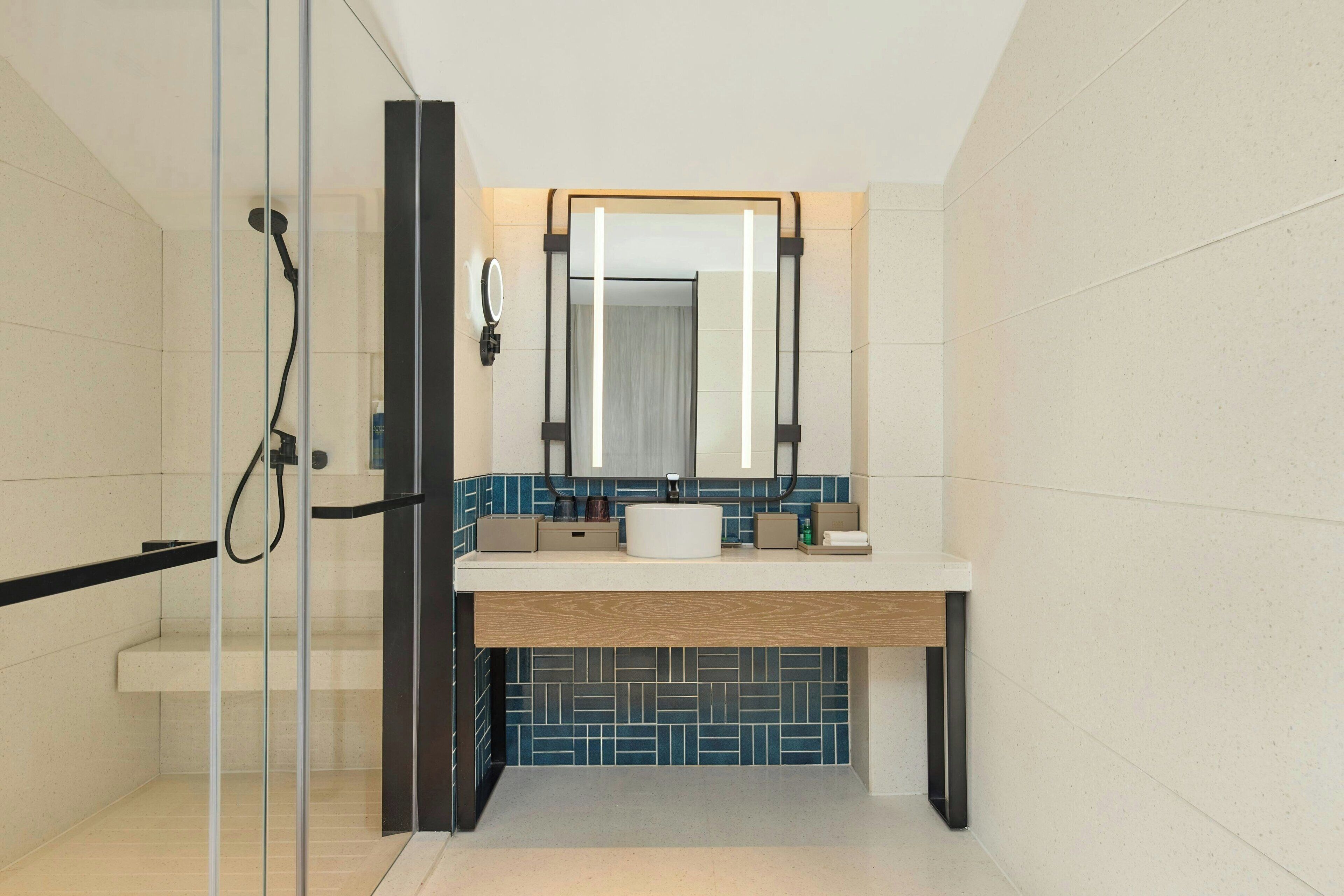 A modern bathroom with a glass shower enclosure, a white sink with a wooden countertop, and a blue-tiled backsplash.