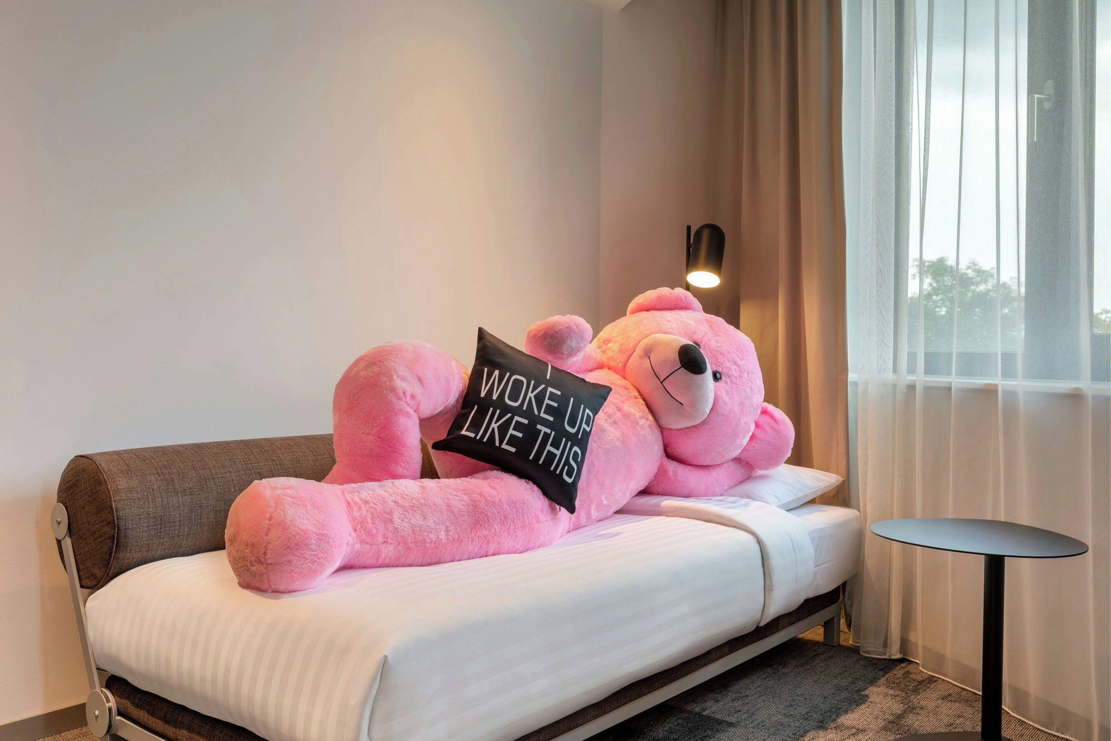 A bed with a large pink teddy bear and a pillow with the text "Woke up like this".