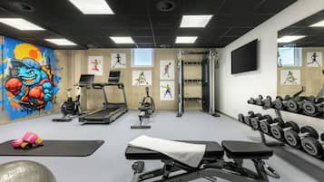 A gym with exercise equipment, a treadmill, dumbbells, and motivational artwork on the walls.