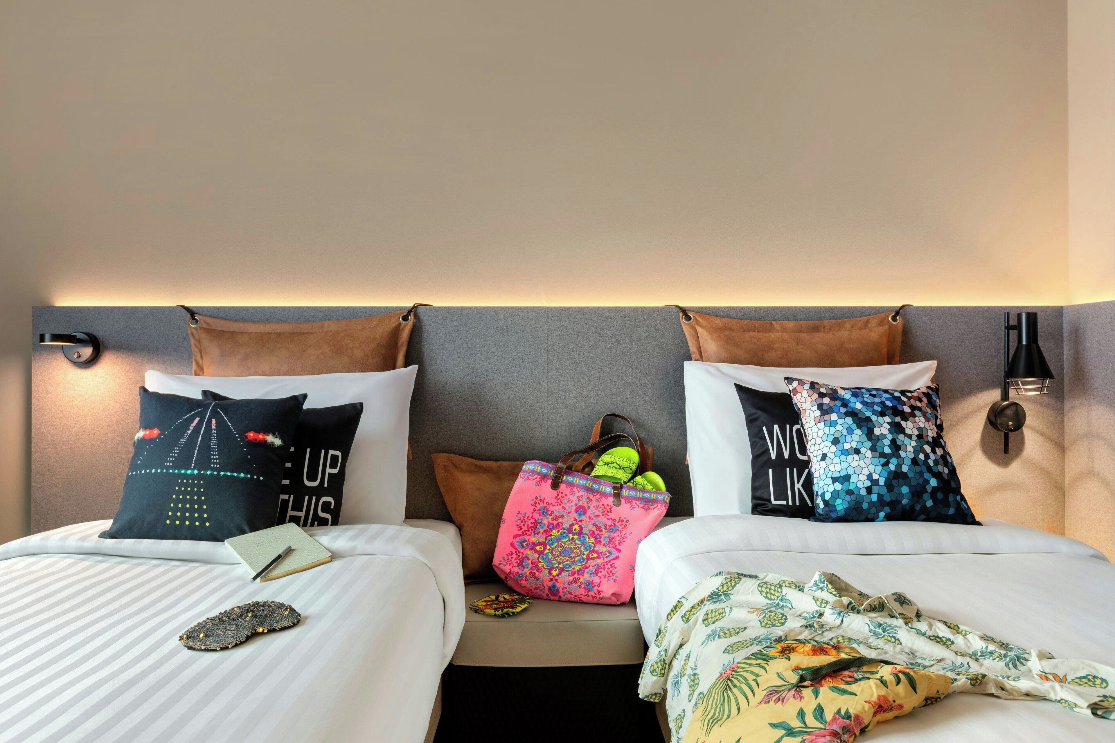 Two beds with pillows, a nightstand, and a lamp.
