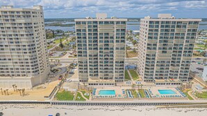 Três edifícios altos com varandas, uma piscina e uma área de praia.