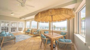 Um pátio amplo com mesa de madeira, cadeiras de vime e um guarda-sol de palha.