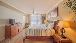 Quarto com cama, cômoda de madeira, televisão e vista para o oceano pela janela.