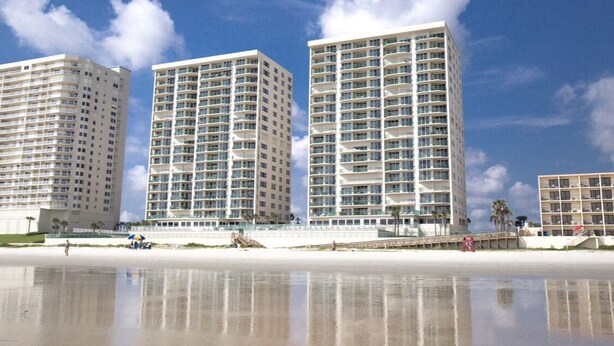 Um hotel à beira-mar com vários edifícios altos, uma praia de areia e céu claro.