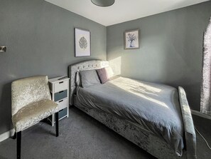 Un dormitorio con cama, una silla, una mesita de noche y dos cuadros en la pared.