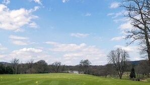 Un campo de golf con cielo despejado, un lago en la distancia y un paisaje ondulado.