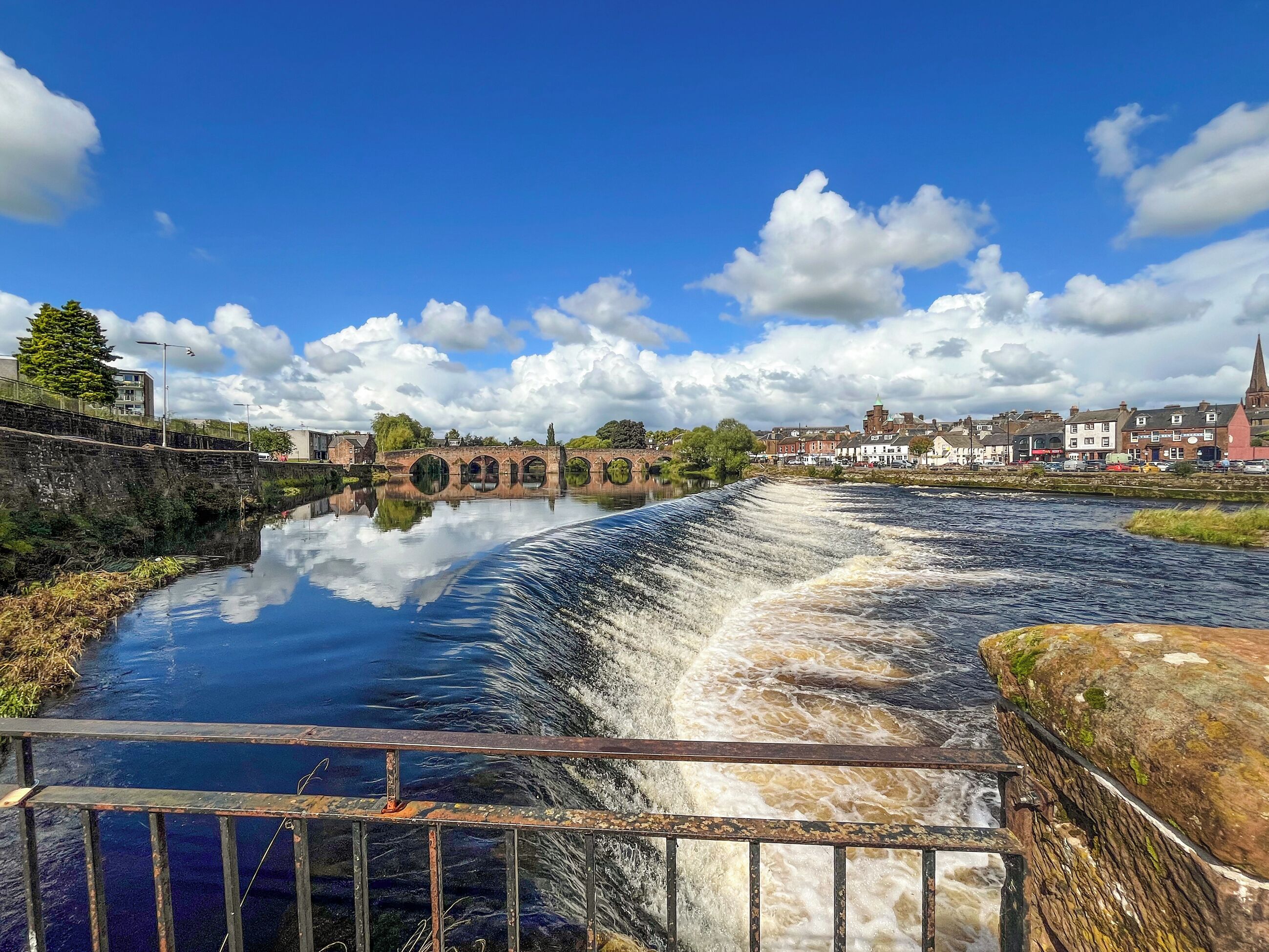Une rivière avec un pont, une ville en arrière-plan et un ciel dégagé.
