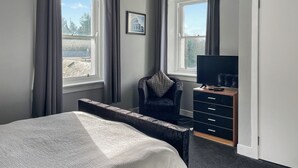 Un dormitorio con cama, una silla, un aparador y un televisor.