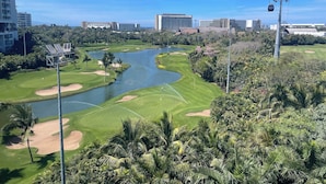Un campo da golf con specchio d'acqua, palme e edifici urbani sullo sfondo.