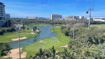 A golf course with a water body, palm trees, and urban buildings in the background.