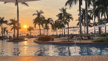A wooden deck with a pool, palm trees, and umbrellas.