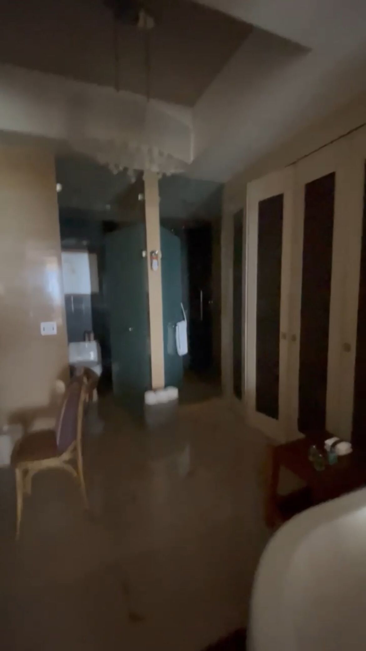 A dimly lit hallway with a chair, a table with items, and a door leading to another room.