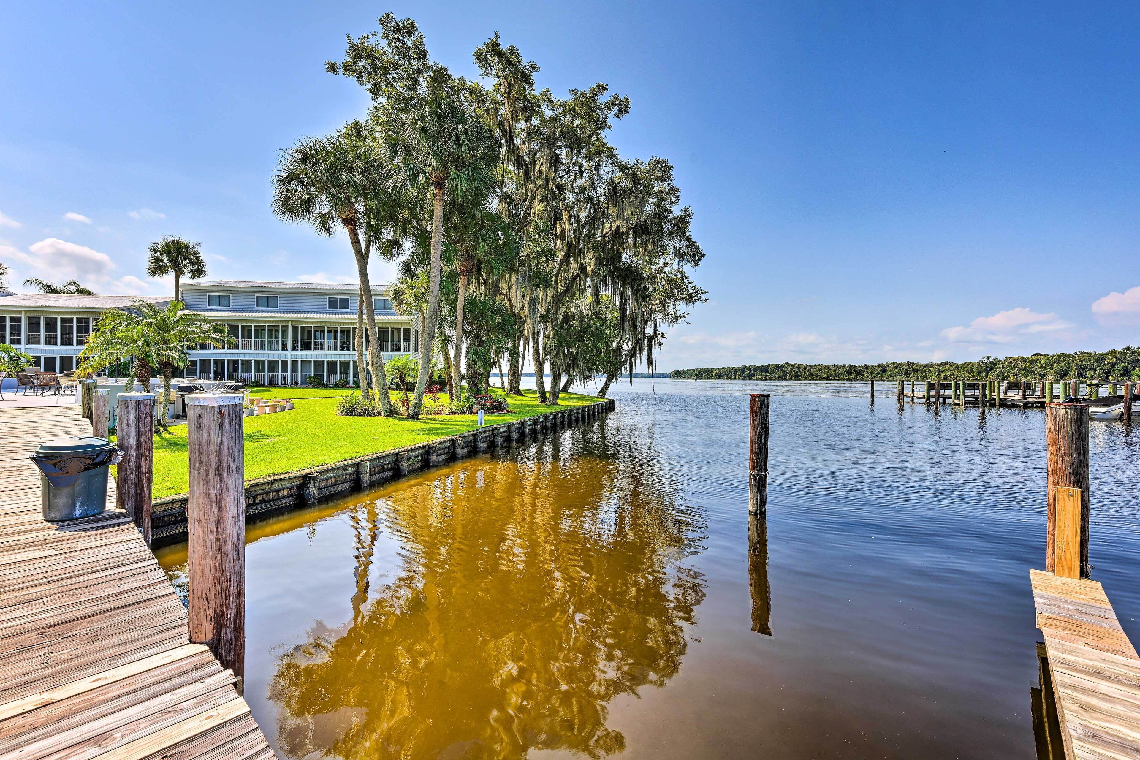 Ein Hotel am Wasser mit einer Holzsteganlage, einem grünen Rasen und einer Baumreihe.