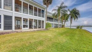 A two-story waterfront property with a covered patio, large windows, and palm trees. - River-View Condo w/ Boat Slip in Welaka! (Welaka)