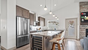 Una cocina moderna con refrigerador de acero inoxidable, armarios de madera, un enfriador de vino y una chimenea de piedra.