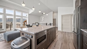 Una cocina moderna con una isla grande, electrodomésticos de acero inoxidable y vistas a un paisaje montañoso a través de amplios ventanales.