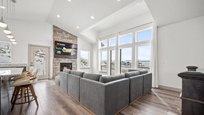 Una sala de estar moderna con un sofá seccional gris grande, una chimenea y un televisor montado sobre una pared de piedra.