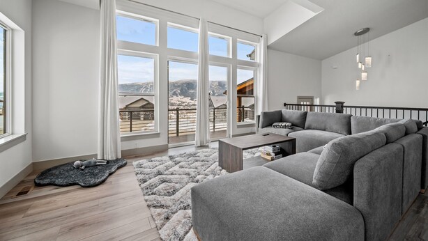 Un salón espacioso con un amplio sofá seccional gris, una mesa de centro de madera y vistas a las montañas a través de amplias ventanas.