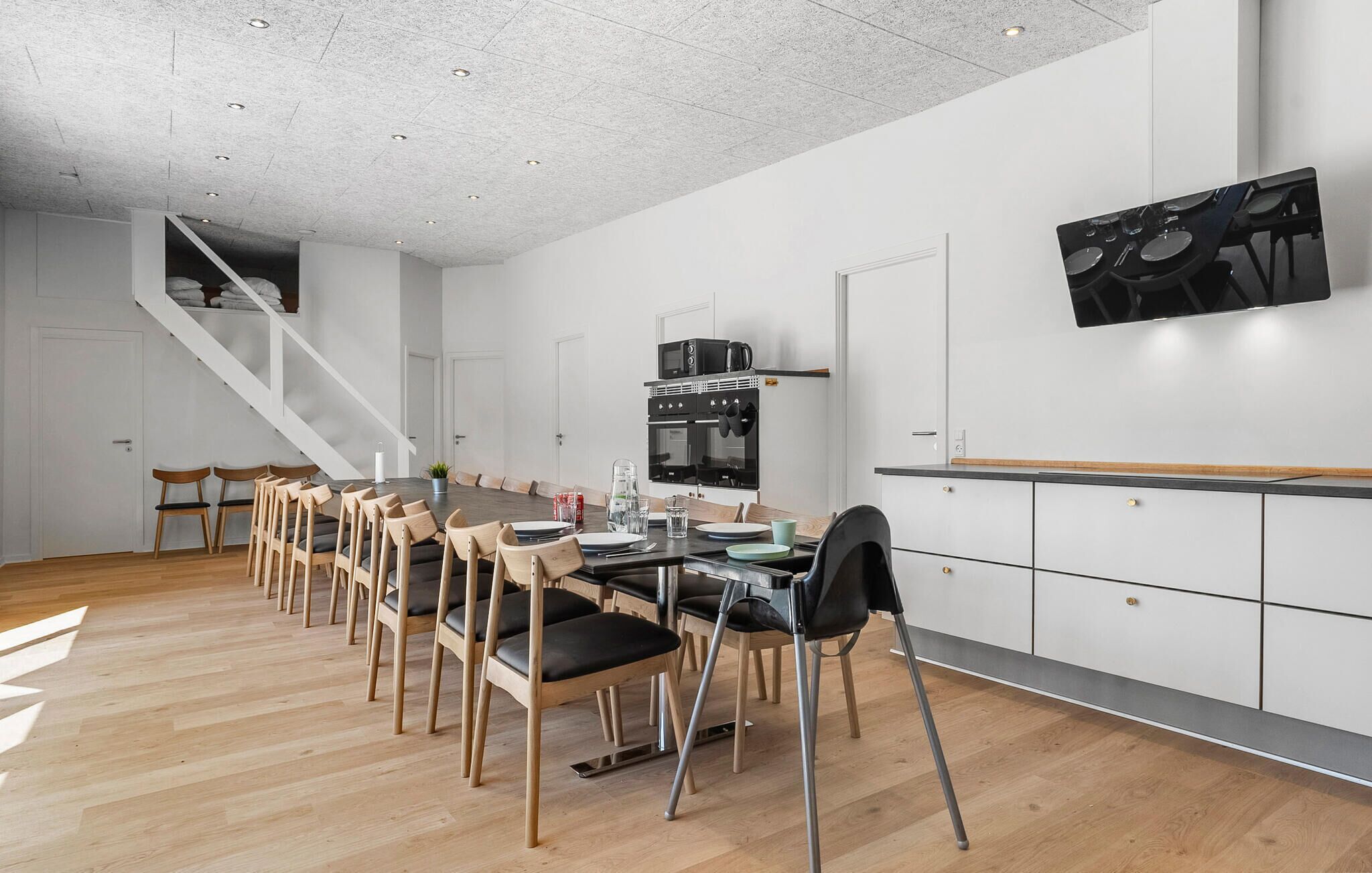 Et moderne køkken med spiseplads, træstole, indbygget ovn og en trappe.