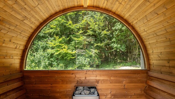 Une cabane en bois dotée d’une grande fenêtre en arc de cercle donnant sur une forêt.