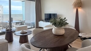 A modern living room with a round dark wood table, white sofas, a TV on a white cabinet, and a balcony with a view of the city. - Lovely apartment in Oostende (Oostende)