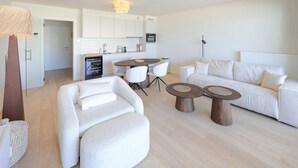 A modern living room with a sofa, two round coffee tables, and a dining area with a table and chairs. - Lovely apartment in Oostende (Oostende)