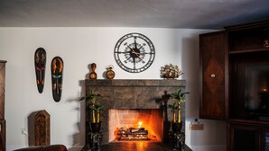 Una chimenea con fuego de leña, un adorno de pared con brújula y dos máscaras colgadas.