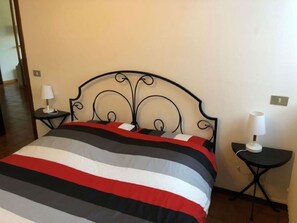 Una cama con estructura metálica negra y colcha a rayas. Hay dos mesitas de noche, cada una con una lámpara blanca.