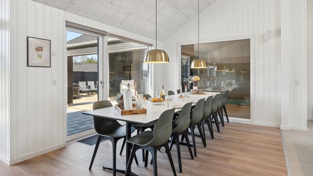 Un espace de salle à manger moderne avec une longue table, des chaises noires et des luminaires suspendus.