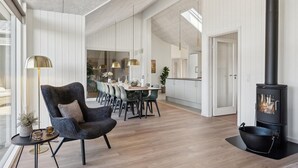 Un vaste espace de vie agrémenté d’une cheminée moderne, un coin repas avec une table et des chaises hautes, et un coin salon confortable avec un fauteuil moelleux et une table d’appoint.
