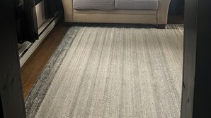 A living room with a beige sofa, patterned cushions, a dark wall, a window with blinds, and a ceiling fan. - The Sasquatch Hideaway: Private 1BR Adventure Loft (Fayetteville)