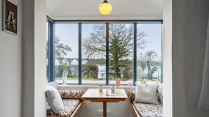 Une pièce avec une grande fenêtre, une table en bois et un banc avec des coussins.