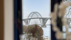 Une vue d’un grand pont en acier enjambant une étendue d’eau, prise à travers une fenêtre dont le premier plan est flou.