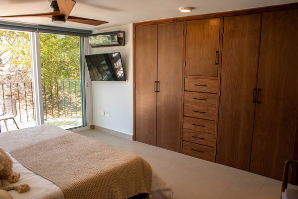 Un dormitorio con un armario grande, una cama, un televisor y un ventanal corredero al exterior.
