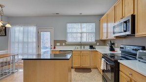 Una cocina moderna con armarios de madera, una isla central, electrodomésticos de acero inoxidable y un amplio ventanal que proporciona luz natural.