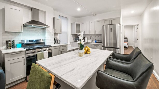 A modern kitchen with white cabinetry, stainless steel appliances, and a marble island with seating.