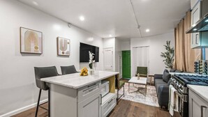 A modern kitchen with a central island, a dining area with chairs, a sofa, and a TV mounted on the wall.