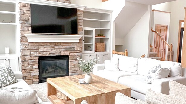 A spacious living room with a stone fireplace, a flat-screen TV, white sofas, and a wooden coffee table.