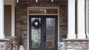 A stone front porch with a dark door, a wreath, and a small table.