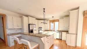 A modern kitchen with white cabinets, a granite countertop, stainless steel appliances, and wooden flooring.