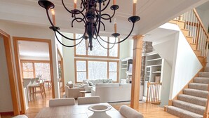 A spacious dining area with a large wooden table, white chairs, and a modern chandelier.