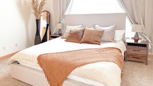 A bedroom with a bed, bedside tables, a lamp, and a vase with dried plants.