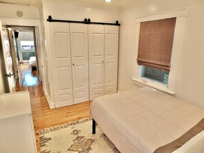Une chambre à coucher comprenant un lit, une fenêtre avec un store, une armoire et une porte donnant sur une autre pièce.